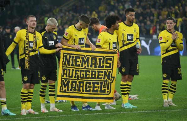 Die Spieler des BVB halten vor der Südtribüne ein Plakat in der Hand, darauf steht: "Niemals aufgeben, Marcel!".

